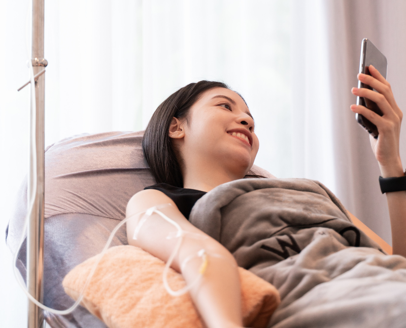 smiling woman holding phone while having iv therapy