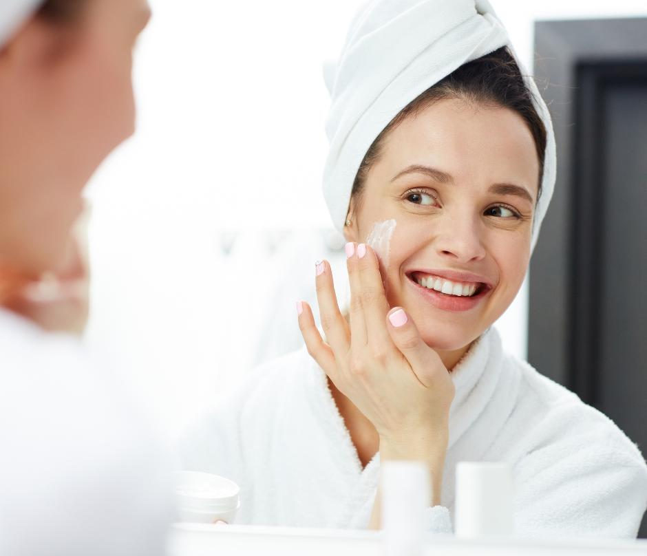 woman applying cream to her face while smiling in the mirror