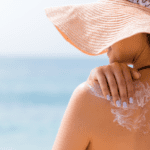 woman with a hat applies lotion to her shoulder