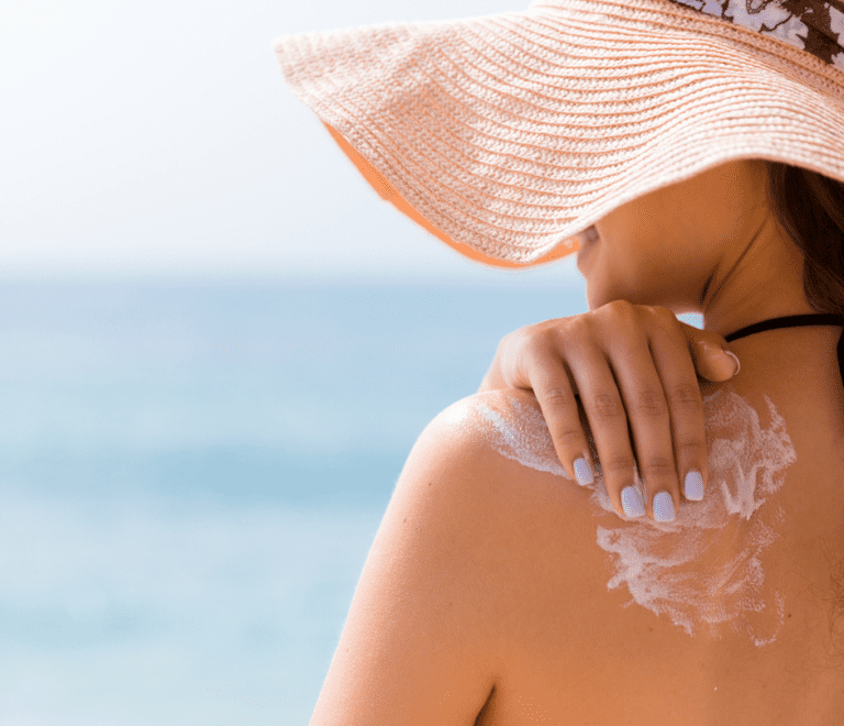 woman with a hat applies lotion to her shoulder
