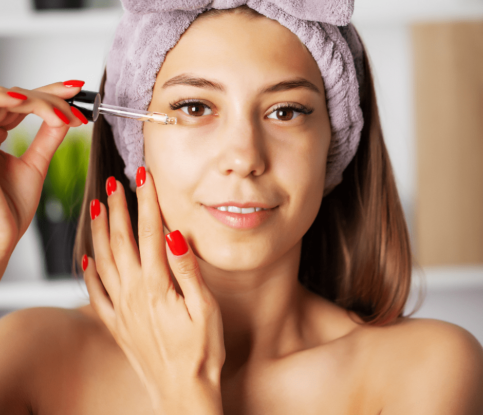 a woman with red nails applying vitamin c serum on her face