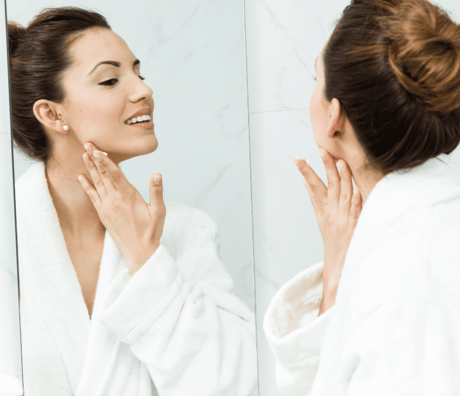 woman putting cream on her face while looking at the mirror