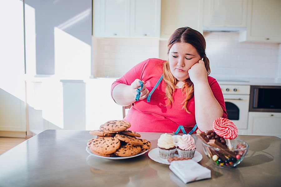 overweight woman looking at her size measurements while sweets are on the table