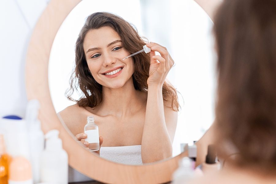 woman looking in the mirror holding a serum with glowing skin