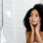 woman looking in the mirror while touching her face comtemplating if she needs cheek fillers