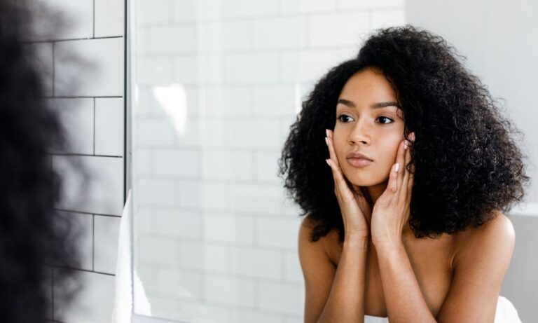 woman looking in the mirror while touching her face comtemplating if she needs cheek fillers