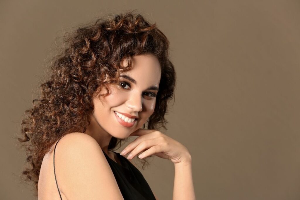 A woman with curly hair smiles warmly, illustrating the benefits of IV hydration discussed in our IV therapy guide.