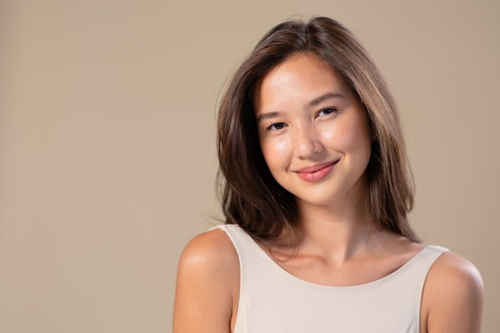 Woman smiling against a neutral background, promoting healthy skin and encouraging clients to get IV therapy for hydration and energy support.