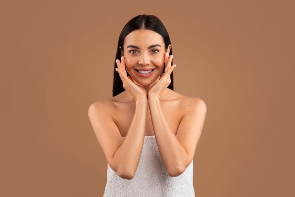 Relaxed woman in a towel touches her cheeks, representing refreshed skin after clients get IV therapy for hydration and recovery.