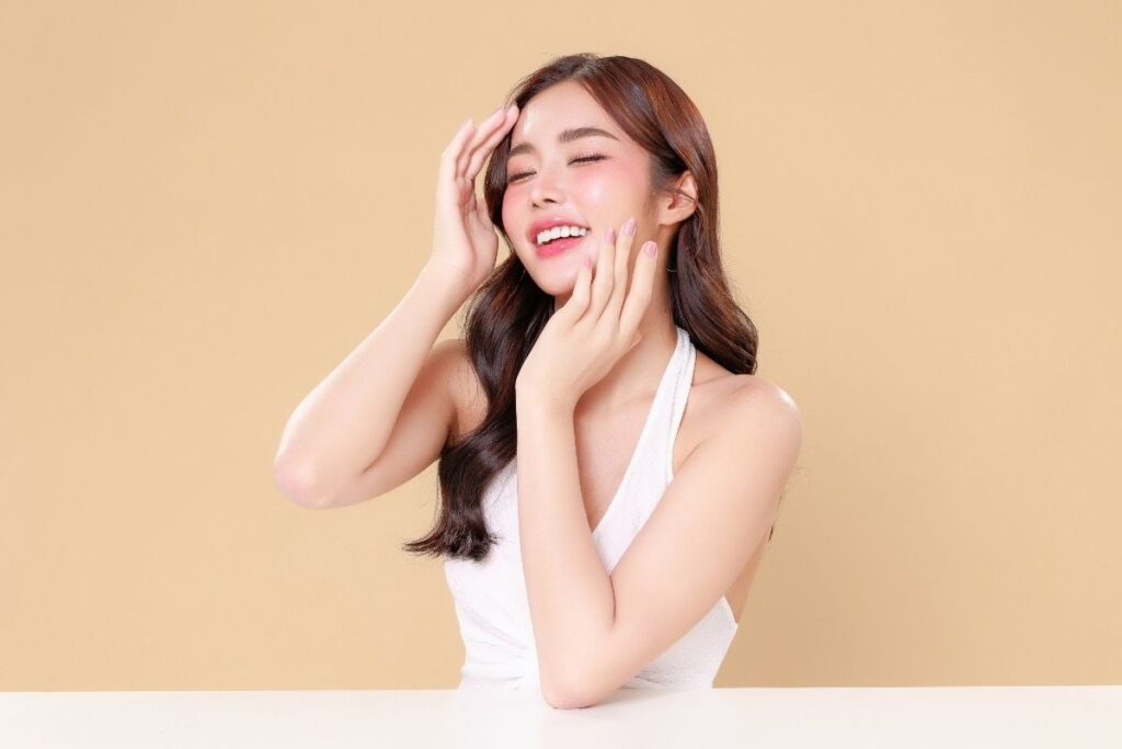 Smiling woman gently touching her face, promoting glowing skin results for those who get IV therapy for hydration and wellness.