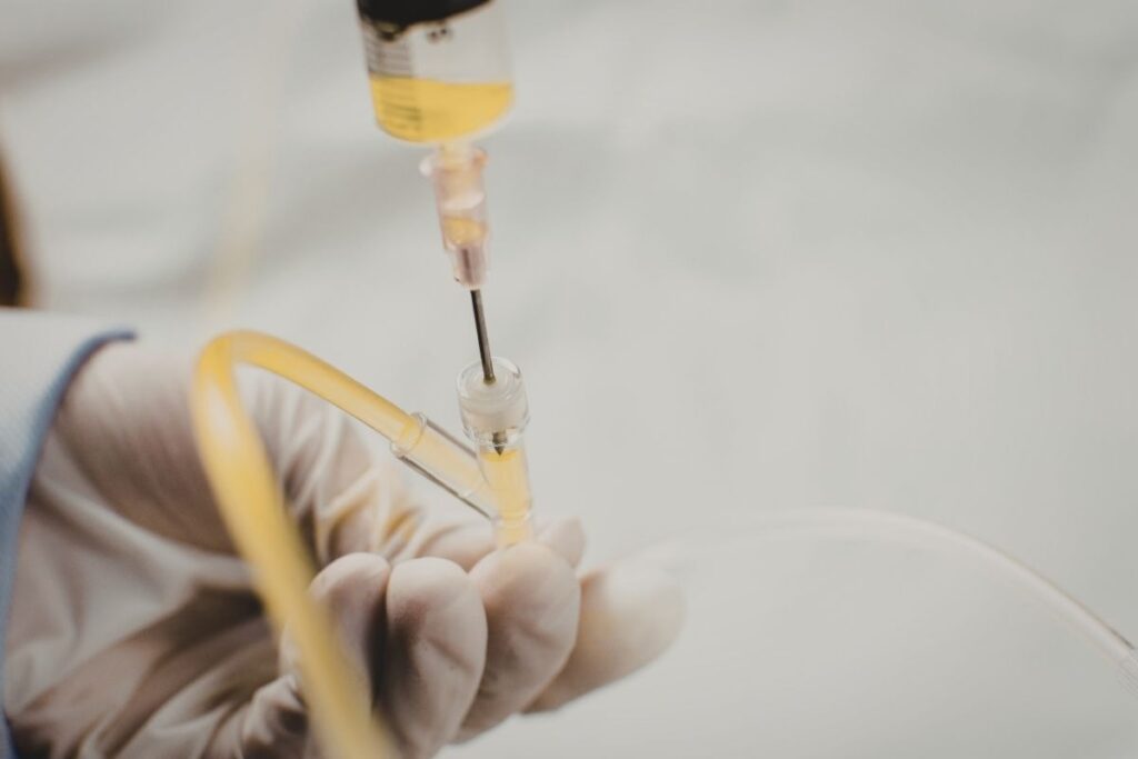 Gloved hand holds syringe with yellow liquid for a first IV infusion guide session.