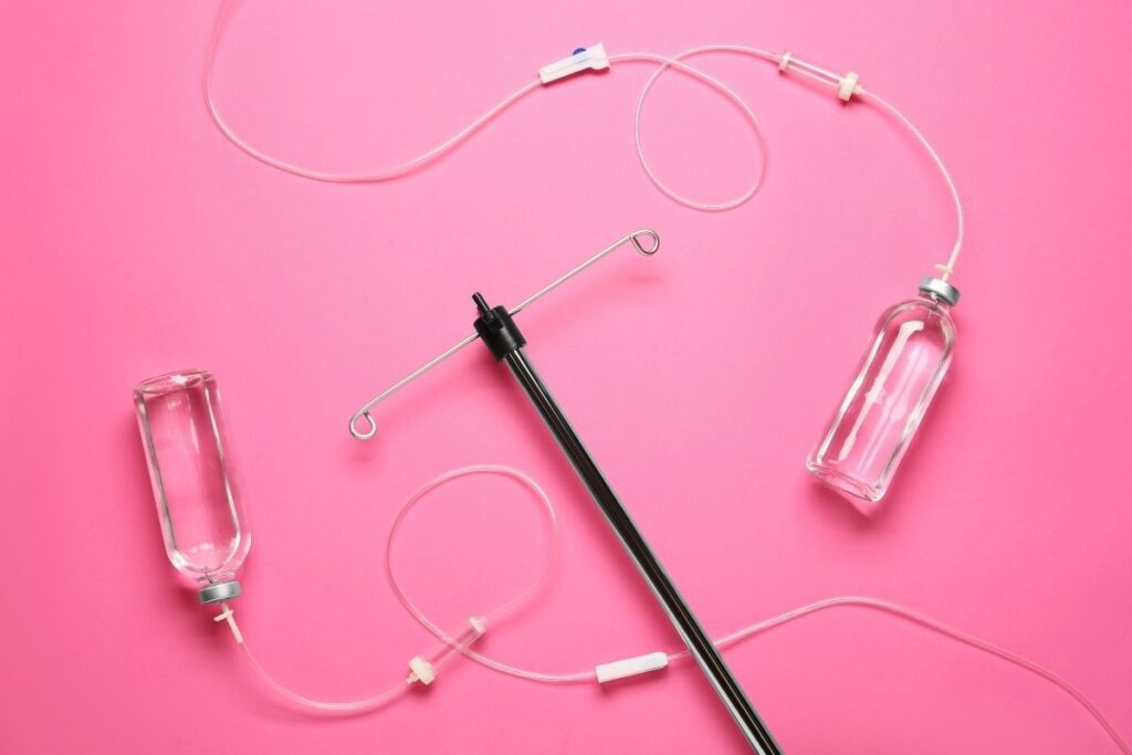 Two clear IV bottles on pink background with IV stand, used in a first IV infusion guide session.