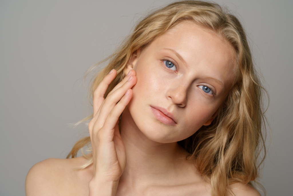 A blonde woman gently touching her cheek in a natural skincare and dermal filler.