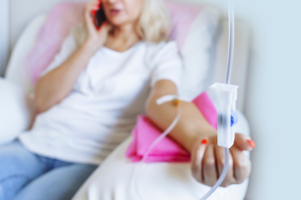 Close-up of an IV drip line with a patient receiving therapy in the background while talking on the phone.