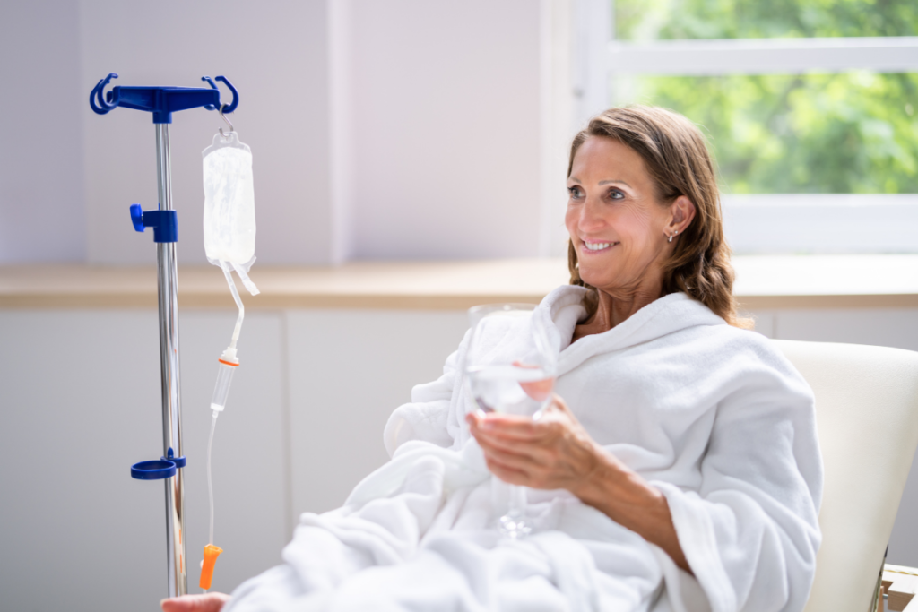 Woman in a white bathrobe relaxing during an IV therapy session beside an IV drip pole.