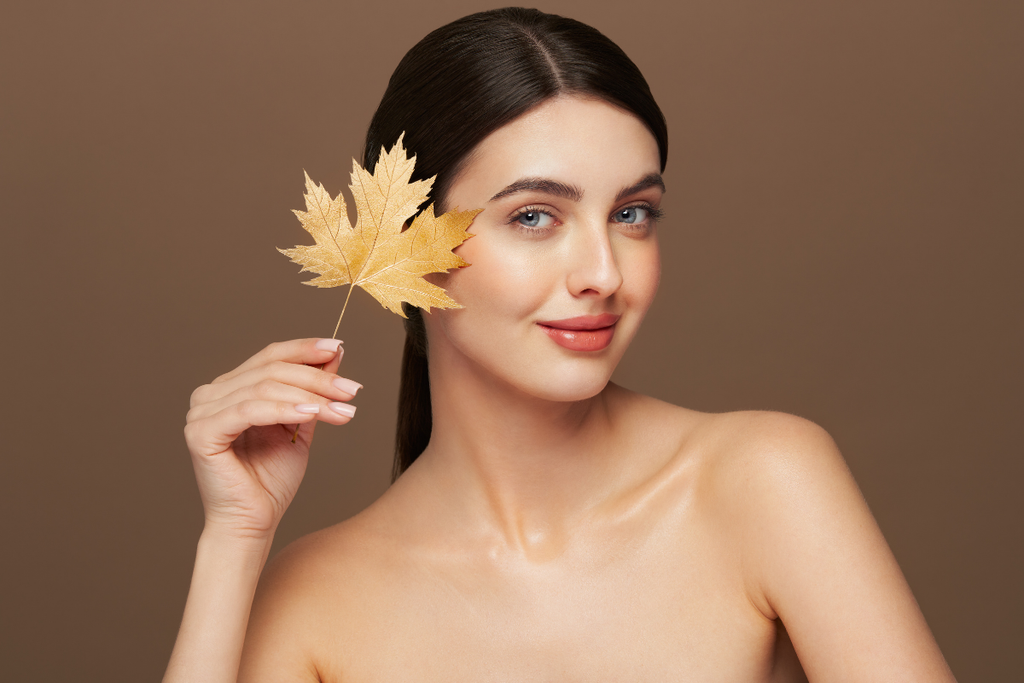 Woman holding a gold leaf next to her face.
