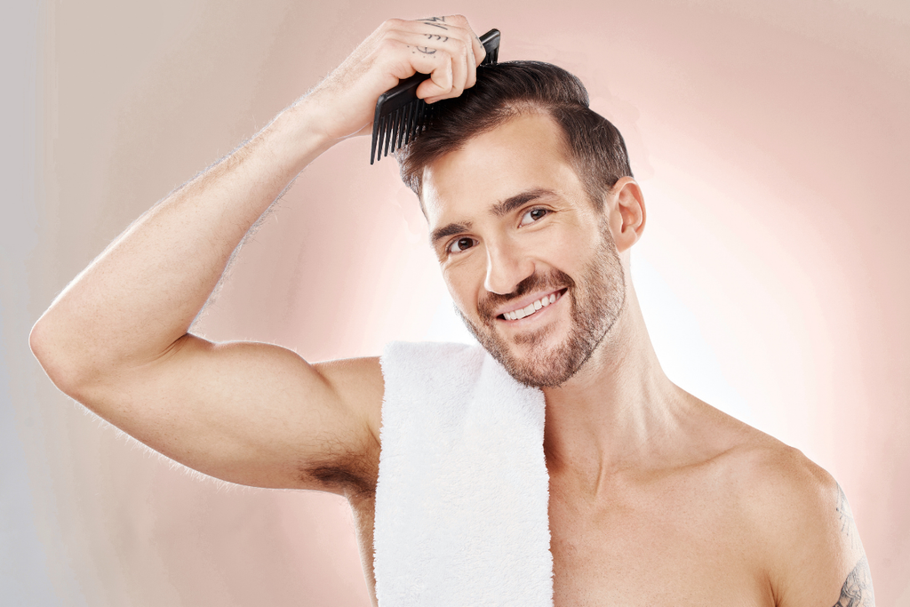 Smiling man combing his hair with a white towel draped over his shoulder.